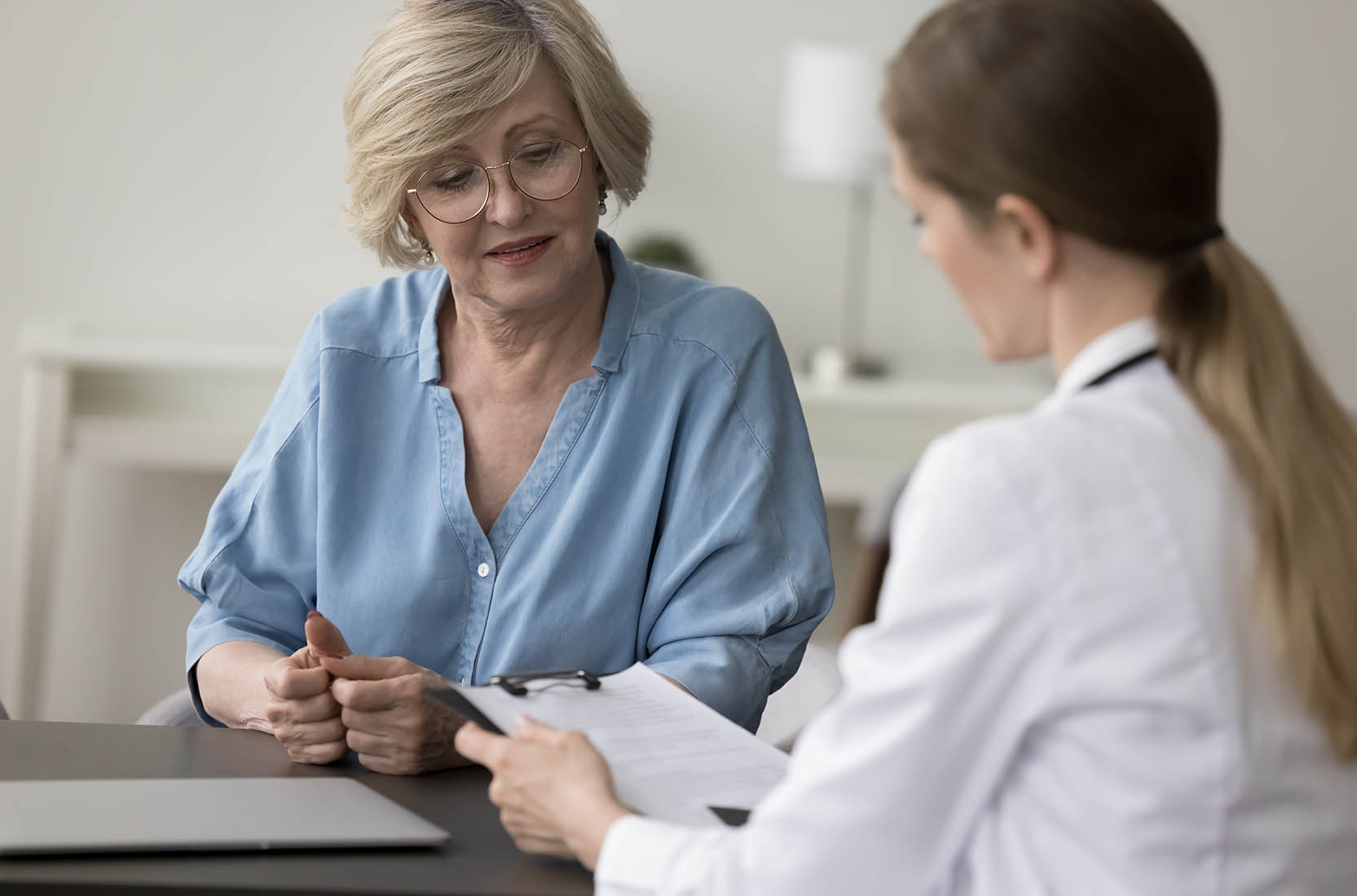 Gp,In,White,Coat,Talk,To,Patient,Seated,At,Desk,